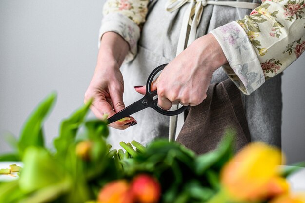 Fleuriste de jeune femme travaillant avec des tulipes de fleurs fraîches, faisant le bouquet. fond blanc