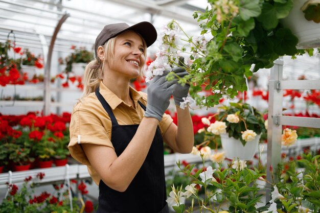 Une fleuriste joyeuse observe les fleurs dans une serre.