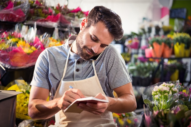 Fleuriste mâle notant l'ordre dans le journal tout en parlant sur téléphone mobile