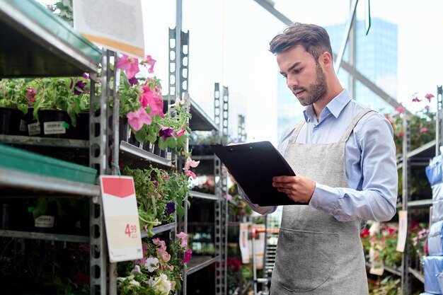 Fleuriste avec presse-papiers debout près d'une étagère avec des fleurs