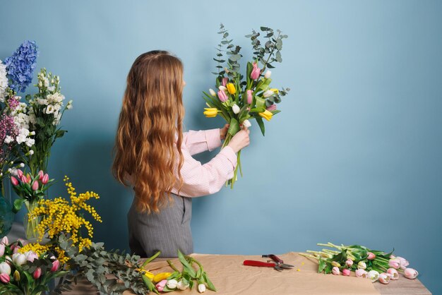 une fleuriste recueille un bouquet de fleurs de tulipes de printemps sur un fond bleu propre