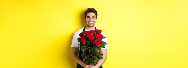 Fleuriste souriant en tablier noir tenant des fleurs vendant un bouquet de roses debout sur un backgro jaune