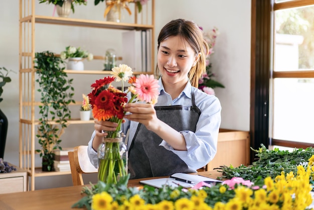 Photo fleuriste en tablier souriant et arrangeant des fleurs de gerbera dans