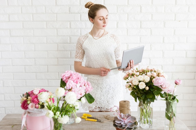 La fleuriste vérifie sa liste de commandes avant le travail. Femme d'affaires avec ordinateur portable en fleuriste. Gestion des petites entreprises, femme gestionnaire, gestion du temps, concept de vente de fleurs en ligne