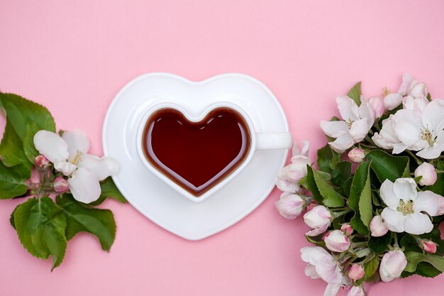 Fleurs blanches et tasse de thé en forme de coeur sur fond rose