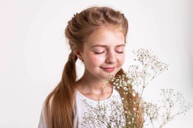 Fleurs blanches touffues. Petite fille tranquille inspirée sentant le parfum des fleurs dans ses mains