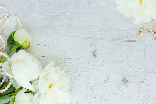 Fleurs et bourgeons de pivoine fraîche blanche avec des bijoux de perles sur le bureau en bois blanc vieilli