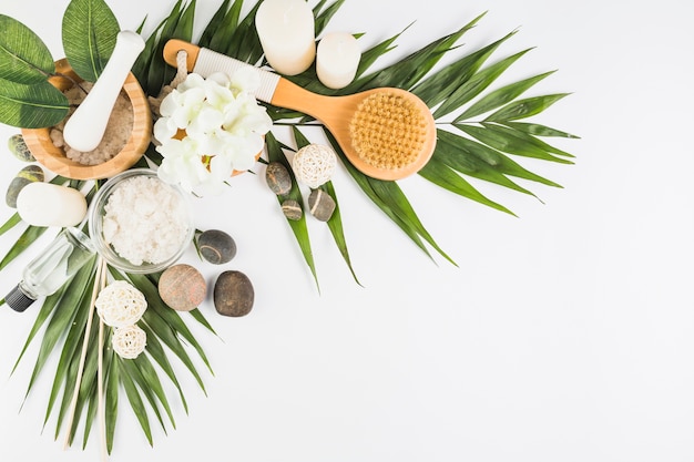 Fleurs; brosse; pierres de spa; sel; bougies; bouteille d&#39;huile sur une surface blanche