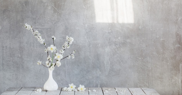 Fleurs de cerisier dans un vase blanc sur la surface vieux mur gris