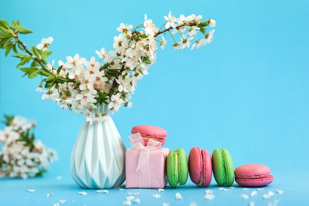 Fleurs de cerisier dans un vase bleu et coffret rose et macarons colorés français sur bleu