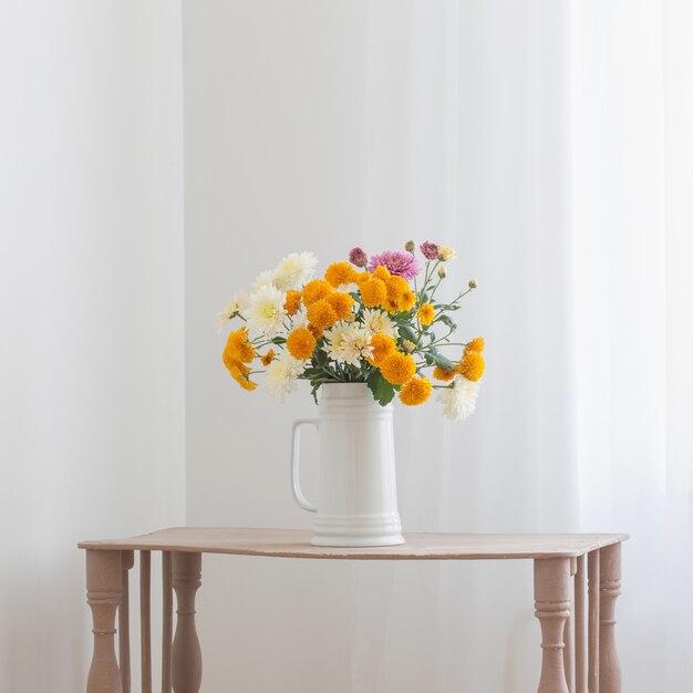 Fleurs de chrysanthème dans une cruche blanche à l'intérieur blanc