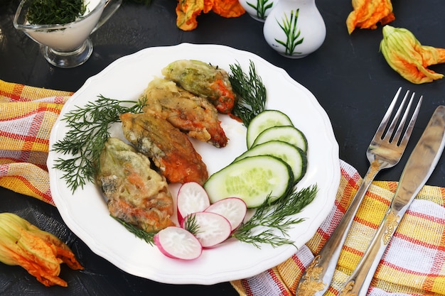 Fleurs de courgettes, cuites en pâte, tranches de concombres et radis sur une assiette