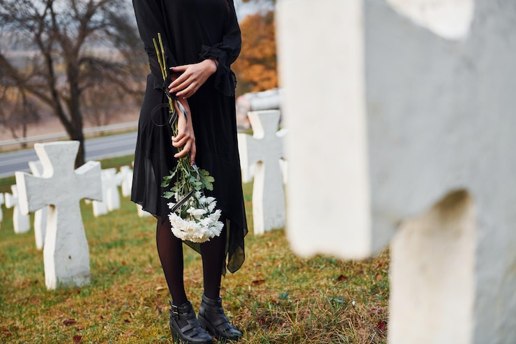 Photo avec des fleurs dans les mains jeune femme en vêtements noirs visitant le cimetière avec de nombreuses croix blanches conception des funérailles et de la mort