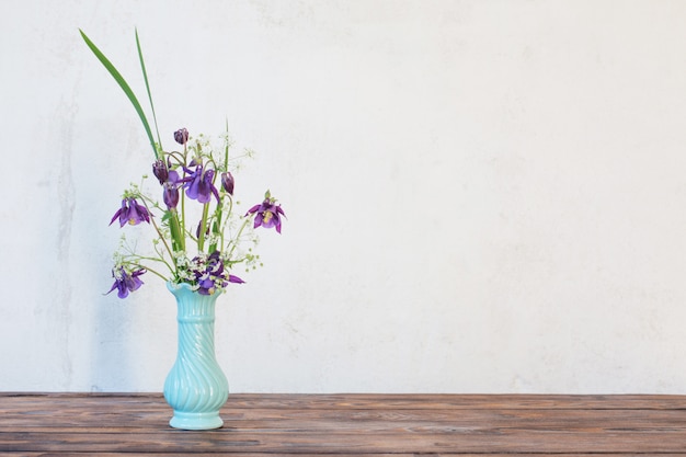 Fleurs dans un vase sur une table en bois sur fond blanc mur