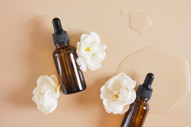 Fleurs d'églantier blanc et bouteille en verre marron avec une pipette sur fond beige, une bouteille d'huile cosmétique ou de sérum sur fond clair humide espace de copie concept de cosmétiques naturels