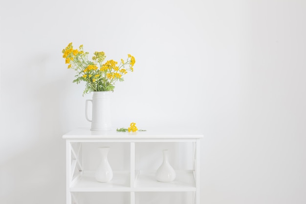 fleurs d'été sauvages jaunes dans une cruche sur un intérieur vintage blanc