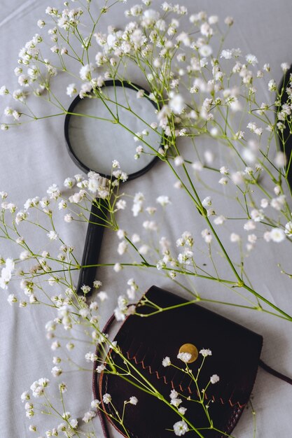 Fleurs de gypsophile blanc, un sac à main pour les pièces et une loupe sur tissu gris