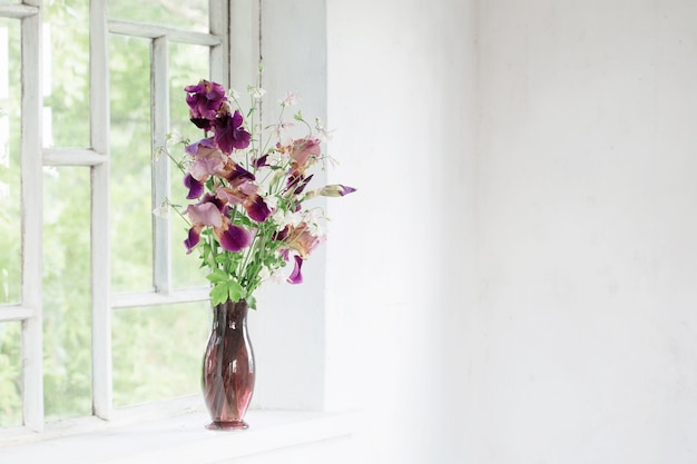 Fleurs d'iris dans un vase en verre sur un vieux rebord de fenêtre blanc