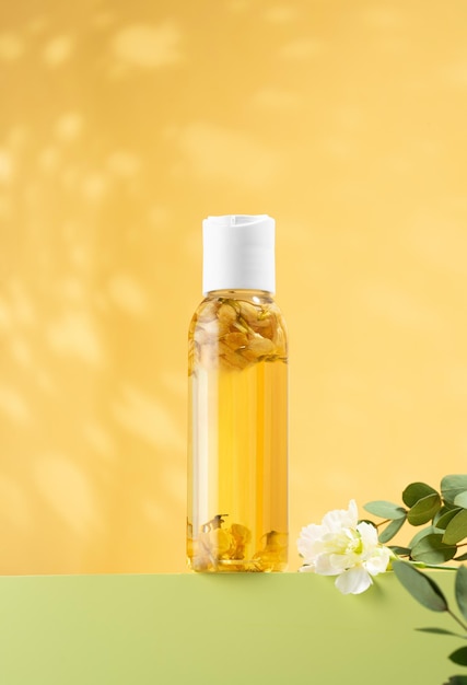 Fleurs de jasmin fraîches à l'intérieur d'une bouteille d'huile essentielle de jasmin debout sur un podium vert clair Huile cosmétique pour bains corporels sur fond jaune Phytothérapie aromathérapie antistress selfcare