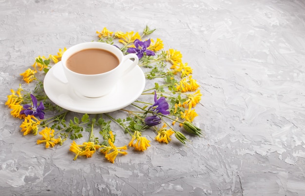 Fleurs jaunes et bleues dans une spirale et une tasse de café sur un béton gris