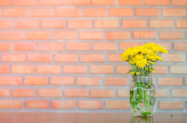 Fleurs jaunes en verre sur table en bois avec fond de brique, espace copie