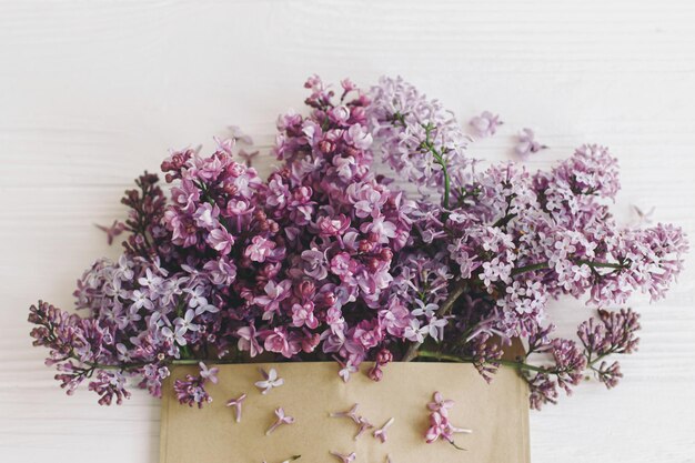 Fleurs lilas dans une enveloppe plate lilas violet en fleurs d'enveloppe artisanale sur bois blanc