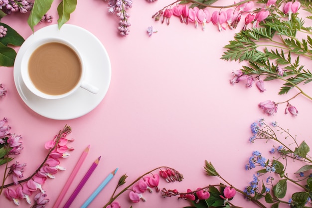 Fleurs lilas violettes et cœur saignant et une tasse de café avec un cahier et des crayons de couleur rose pastel.