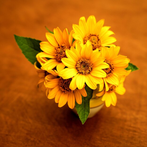 Fleurs lumineuses jaunes dans un vase sur une surface en bois