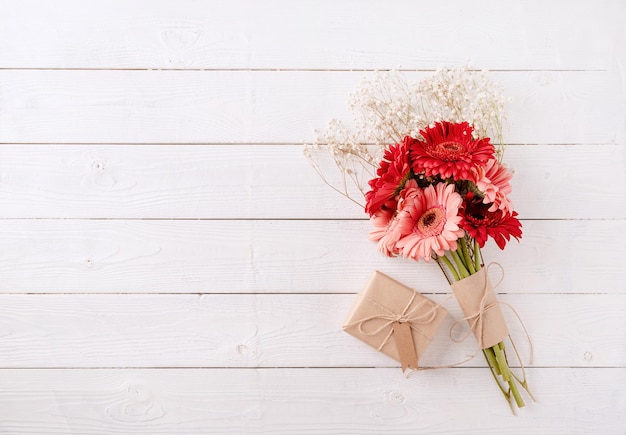 Fleurs de marguerite gerbera rouge et coffret cadeau artisanal avec étiquette sur table en bois blanc