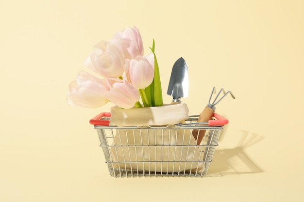 Des fleurs d'outils de jardin dans un sac et un panier d'achat sur un fond clair