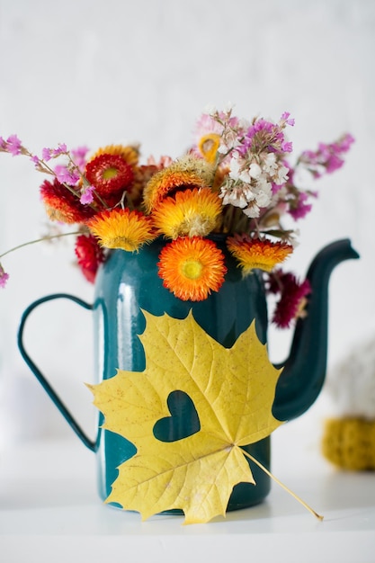 Fleurs de paille d'automne Helichrysum bracteatum dans un bidon d'eau de vase vert vintage et une feuille en forme de coeur jaune Beau bouquet d'automne coloré près d'un mur de briques blanches