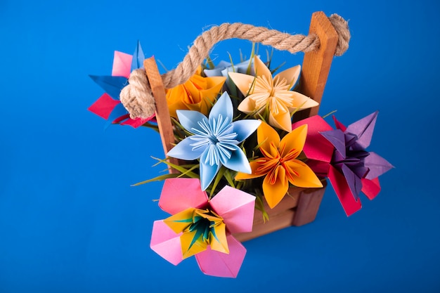 Fleurs en papier de couleur à la main origami bouquet artisanat en papier dans un panier avec de l'herbe en studio sur fond bleu coloré