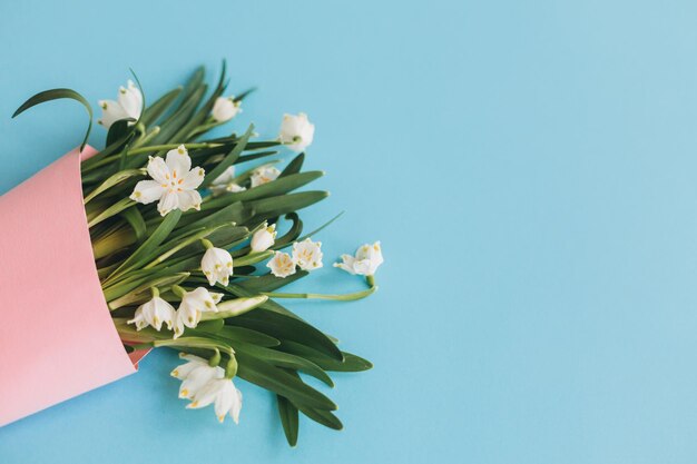 Fleurs printanières blanches dans un cône rose sur fond bleu plat poser Bonjour printemps Carte de voeux élégante Concept de la journée de la femme heureuse Fête des mères heureuse Flocon de neige de printemps Image à la mode florale