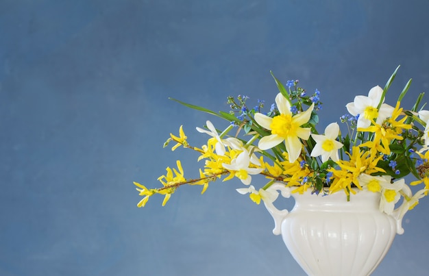Fleurs de printemps blanches et jaunes dans un vase sur une table en bois sur fond bleu