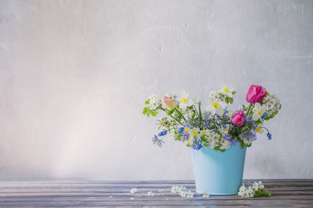 Fleurs de printemps dans un seau bleu sur une surface blanche