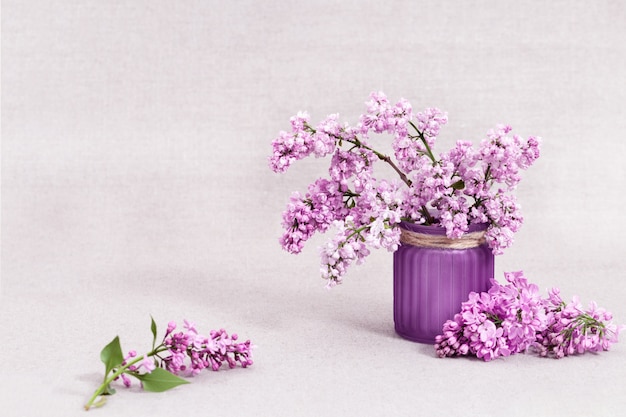 Fleurs de printemps de lilas dans un vase en verre sur une nappe rustique.