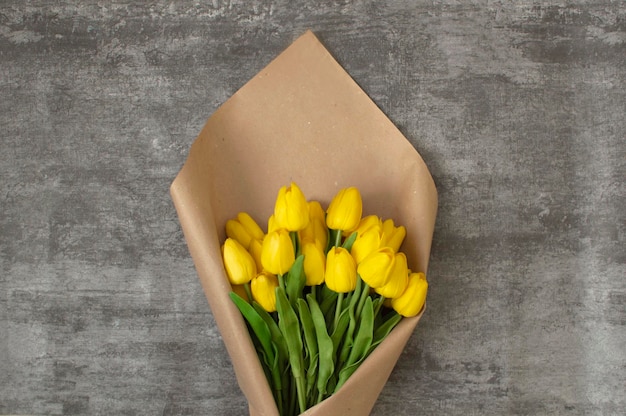 Fleurs de printemps, une tulipe sur fond gris. Belles tulipes jaunes avec un espace pour le texte. Un bouquet de tulipes emballé dans du papier kraft.