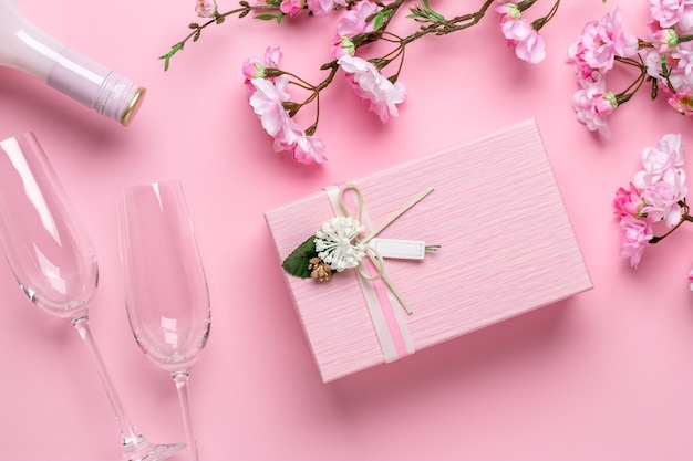 Fleurs de printemps, verres, champagne et coffret cadeau sur fond rose festif. Carte de voeux romantique le jour de la Saint-Valentin. Journée internationale de la femme, célébration le 8 mars.