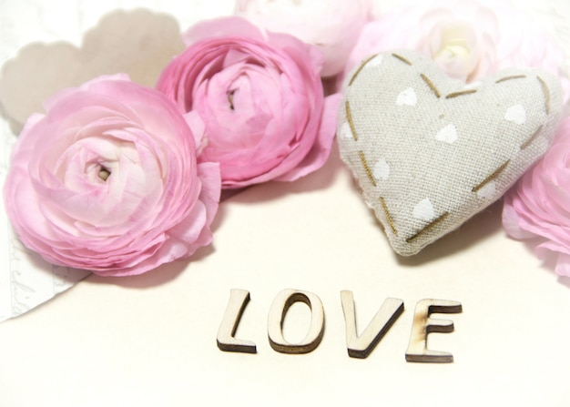 Fleurs de renoncule rose, coeur de tissu et mur d'amour de texte sur un napperon au crochet se bouchent