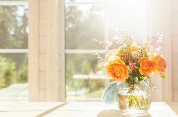 Fleurs roses anglaises orange de la Saint-Valentin dans un bocal en verre sur le fond d'une grande fenêtre d'un espace de maison en bois pour le texte intérieur rétro de style vintage avec des fleurs