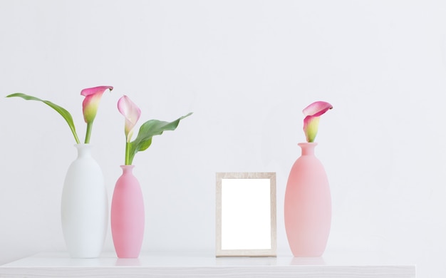 Fleurs roses dans des vases et cadre sur une surface blanche