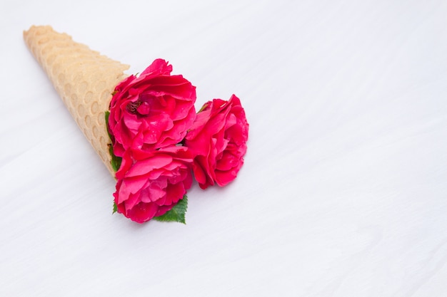 Fleurs roses rouges dans un cône de gaufre sur fond en bois blanc. Mise à plat, vue de dessus, fond floral.