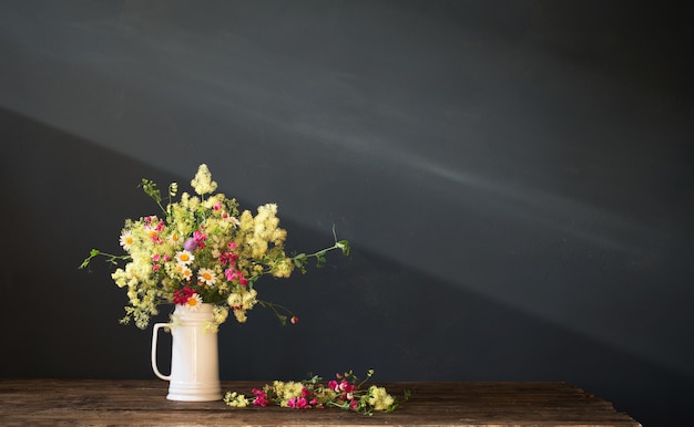 Fleurs sauvages dans une cruche blanche sur une surface sombre