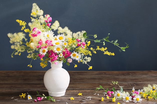 Fleurs sauvages dans un vase blanc sur un mur sombre