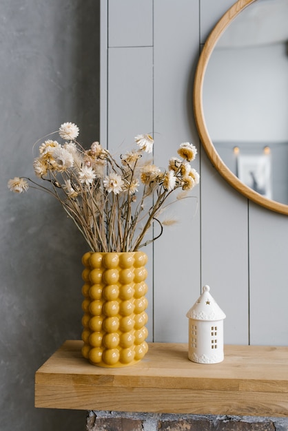 Fleurs séchées dans un vase en céramique jaune dans le décor intérieur d'une maison scandinave aux murs gris.