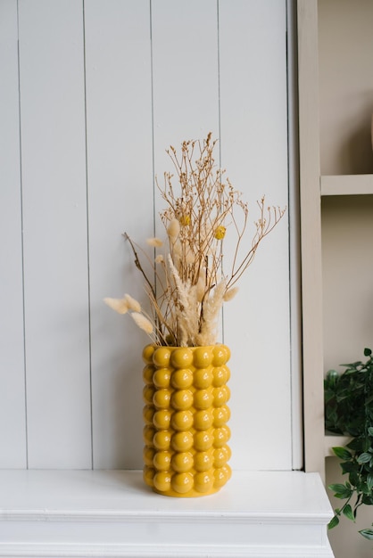 Fleurs séchées dans un vase jaune dans le décor d'une chambre cosy à la maison