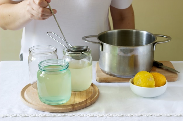 Fleurs de sureau, eau, citron et sucre, ingrédients et une femme préparant un sirop de sureau. Style rustique.