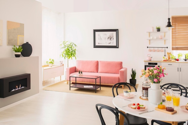 Fleurs à table à l'intérieur de l'appartement blanc avec affiche au-dessus du canapé rose près de la cheminée Photo réelle
