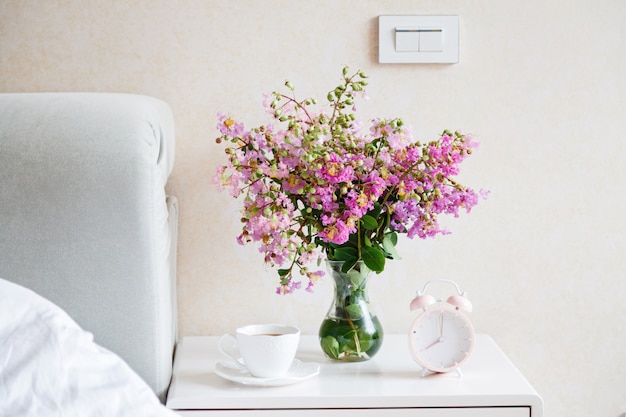 Fleurs, tasse de café et réveil dans la chambre