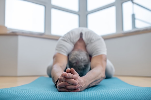 La flexibilité. Un yogi mûr exerçant à la maison et ayant l'air flexible